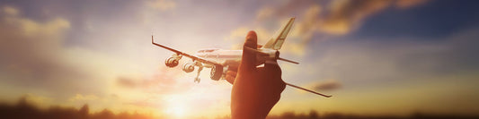 A hand holding a toy airplane against a glowing sunset sky, symbolizing the dream of travel and adventure.