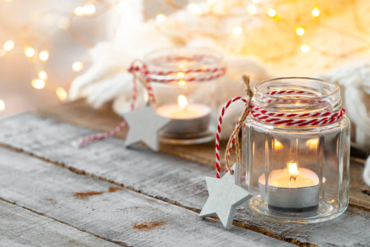 Two small glass jars with lit tealight candles wrapped in red and white twine, adorned with wooden star ornaments, set on a ru