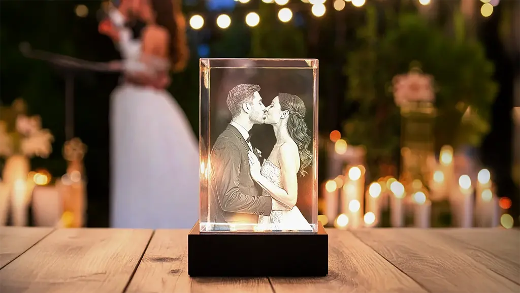 Custom 3D photo crystal keepsake of a bride and groom sharing a kiss, displayed on a wooden surface with bokeh wedding lights