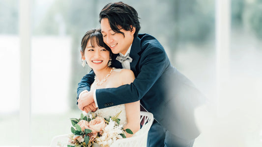 Smiling bride and groom embracing warmly while sitting together, holding a floral bouquet.