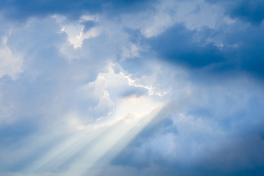 A serene sky with beams of sunlight piercing through fluffy clouds, creating a peaceful and divine atmosphere.