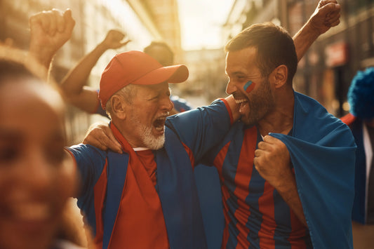 Older man and younger man wearing red and blue fan gear, cheering passionately during a street celebration, with expressions o