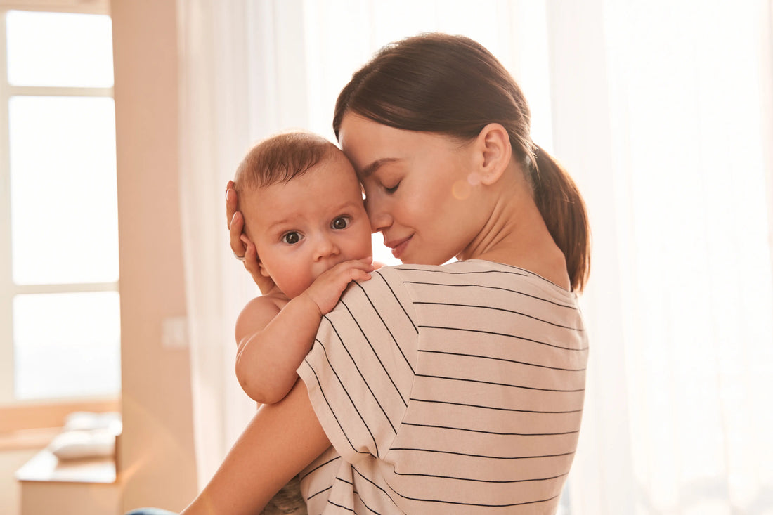 Tender moment between a mother and her baby as she gently holds the baby close to her face in a sunlit room.