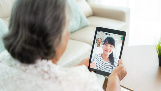An elderly woman using a tablet to video chat with her daughter, both smiling warmly during their virtual conversation.