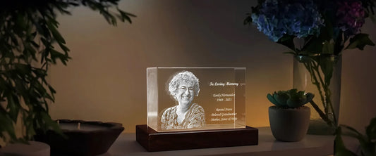 A softly lit room with a glowing 3D memorial crystal showing a smiling woman, engraved with her name, dates, and a tribute, wi