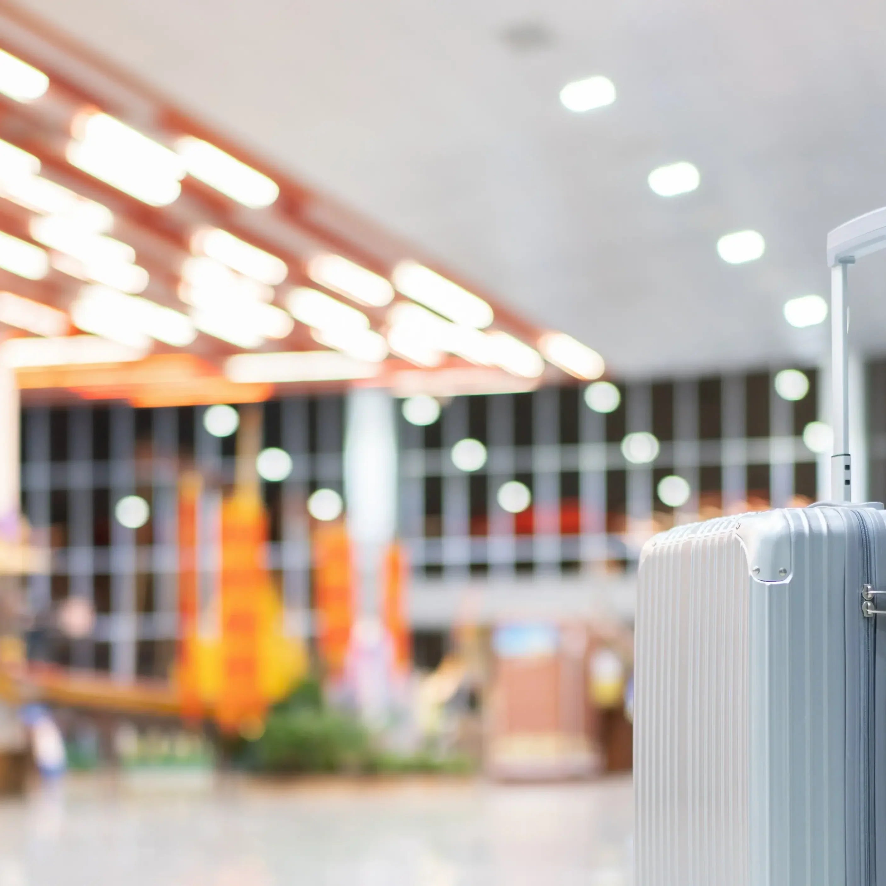 Silver hard-shell suitcase with leather luggage tag attached, alone in a brightly lit modern airport terminal — Beyond Memories luggage tag necessity guide.