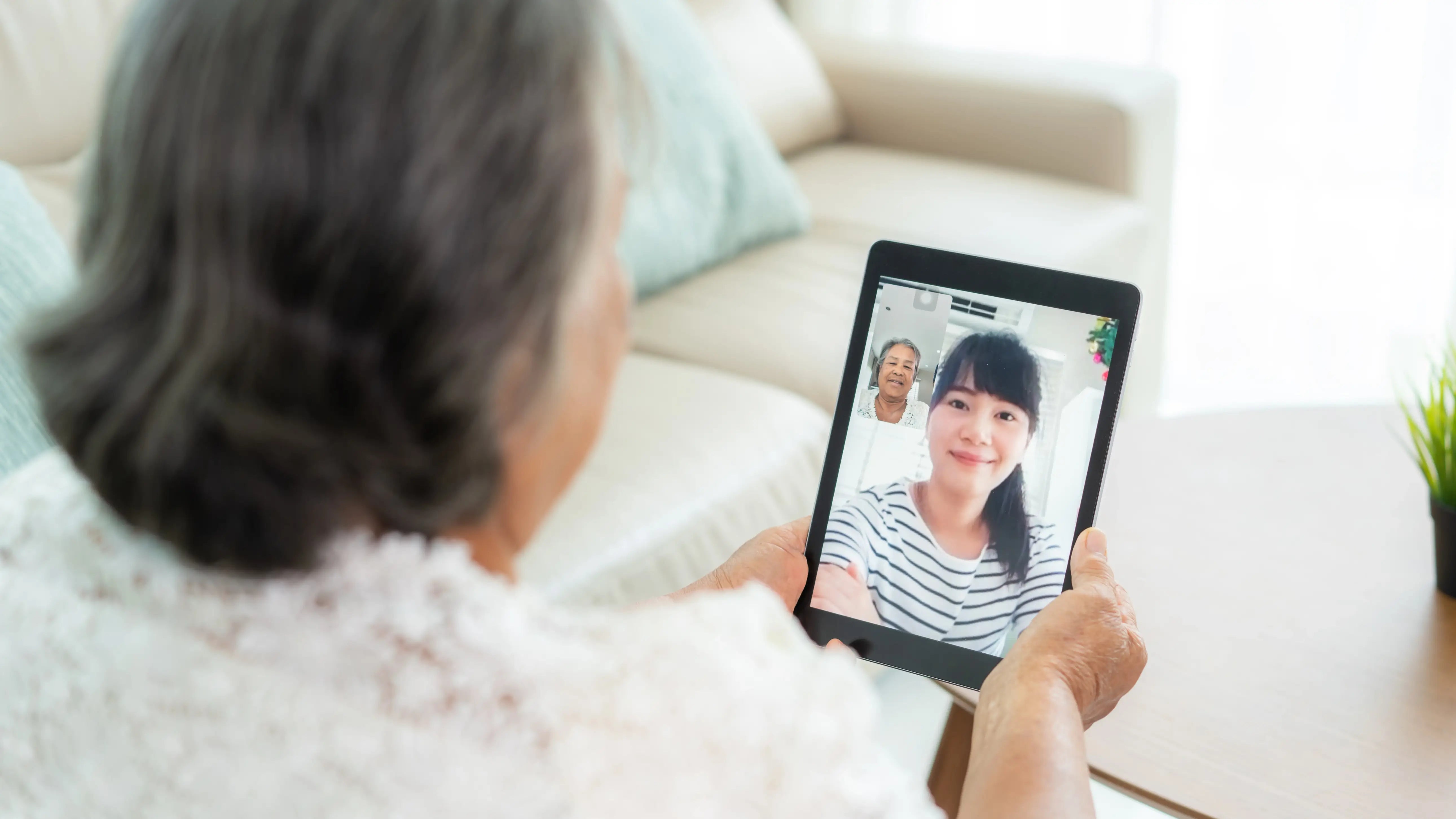  An elderly woman using a tablet to video chat with her daughter, both smiling warmly during their virtual conversation.