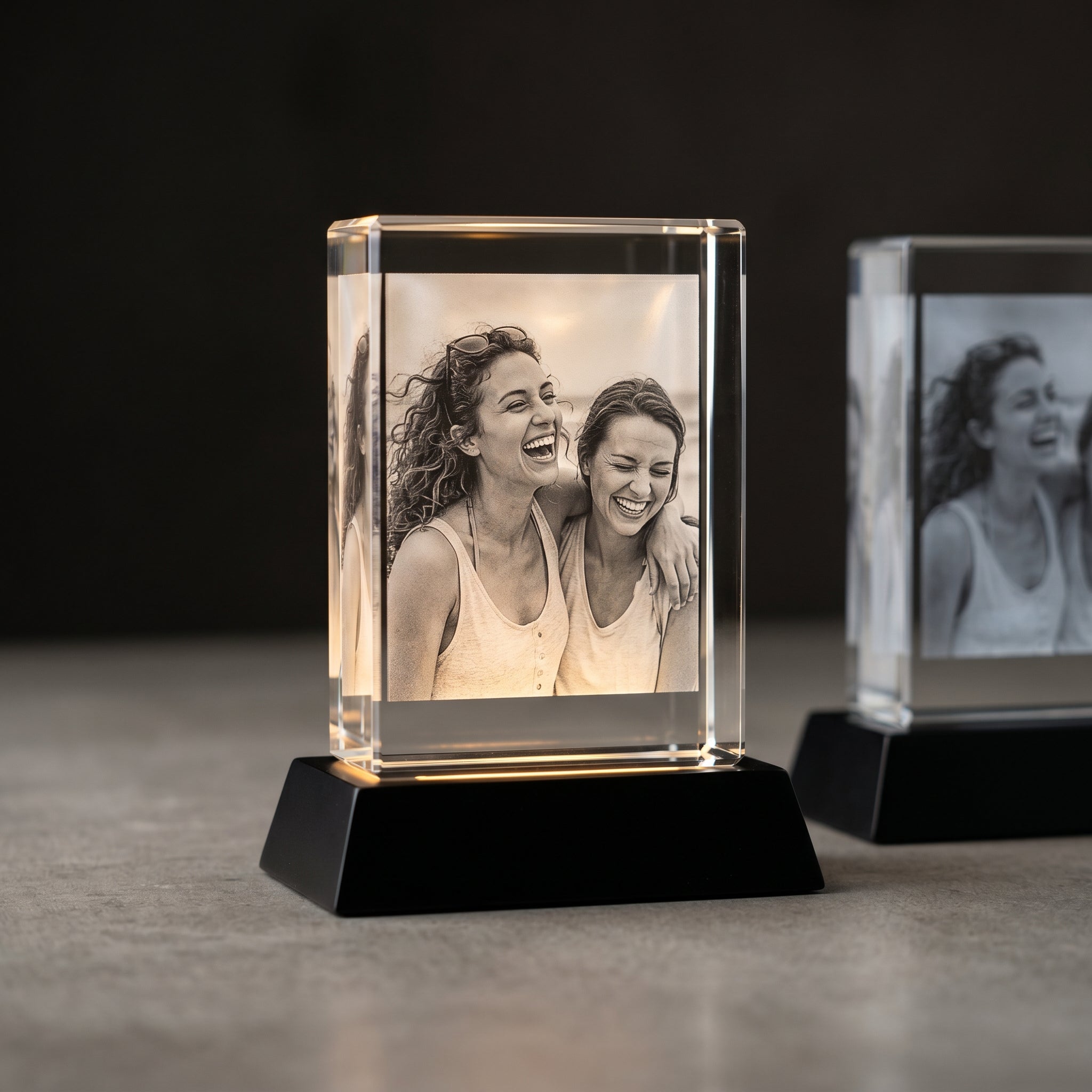 Beyond Memories rectangle 3D crystal in sharp warm focus on the left next to a softer generic comparison crystal on a concrete slab in editorial gallery light.