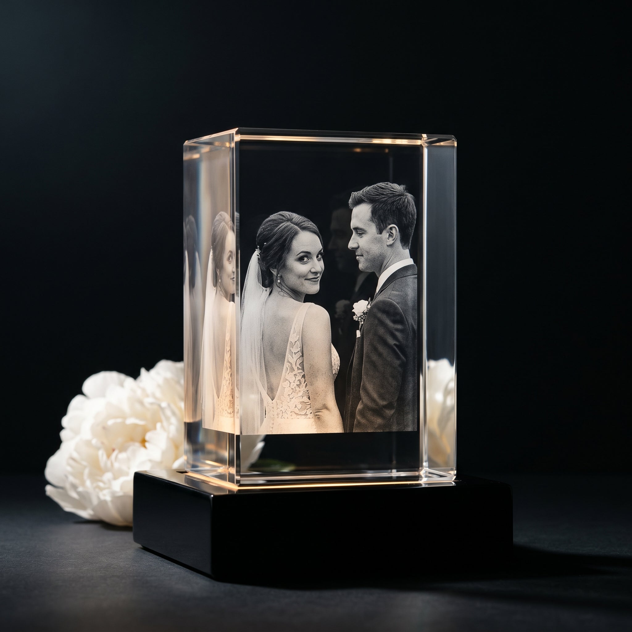 BM rectangle 3D crystal of bride and groom looking at each other on wedding day, black premium base on dark studio with white peony bouquet bokeh, editorial bridal-day mood