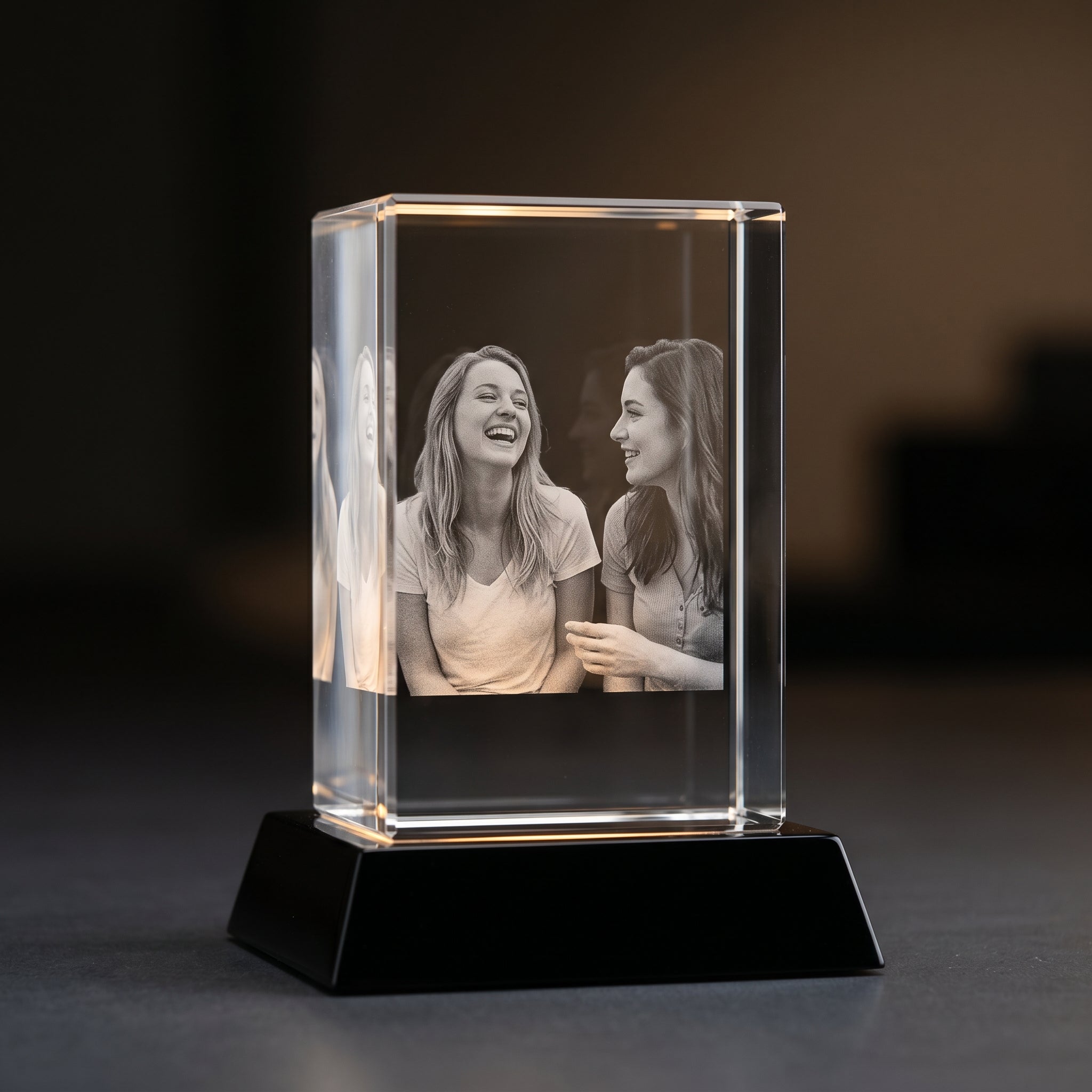 Beyond Memories 3D crystal with engraved candid two friends laughing, on black Premium Wood base with monolithic dark backdrop.